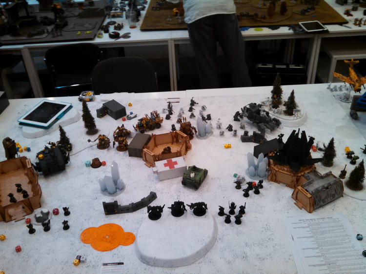 A wide view of the tabletop battlefield, with terrain and miniature forces deployed